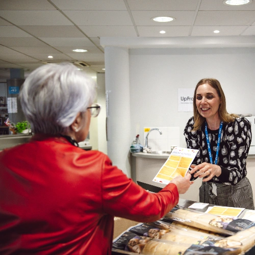 woman behind desk handing another woman a flyer